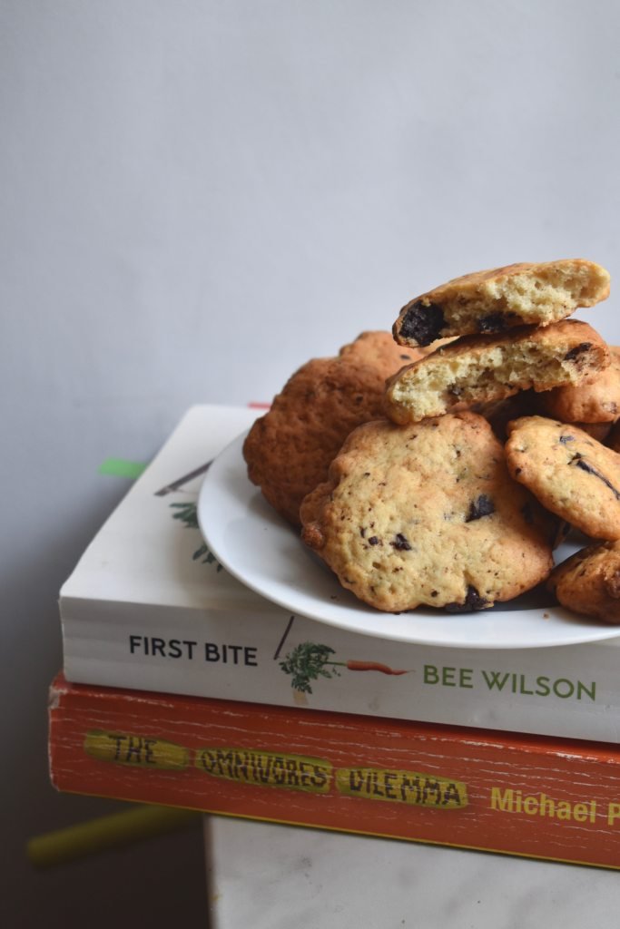 A plate of cookies with chocolate pieces on a pile of books 